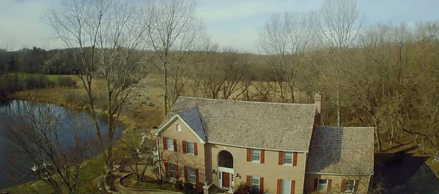 Aerial view of a house beside a pond and leafless trees